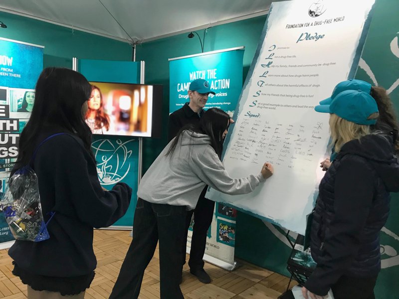 Volunteers encourage youth to sign the drug-free pledge board at the Foundation for a Drug-Free World tent at the Rose Bowl.