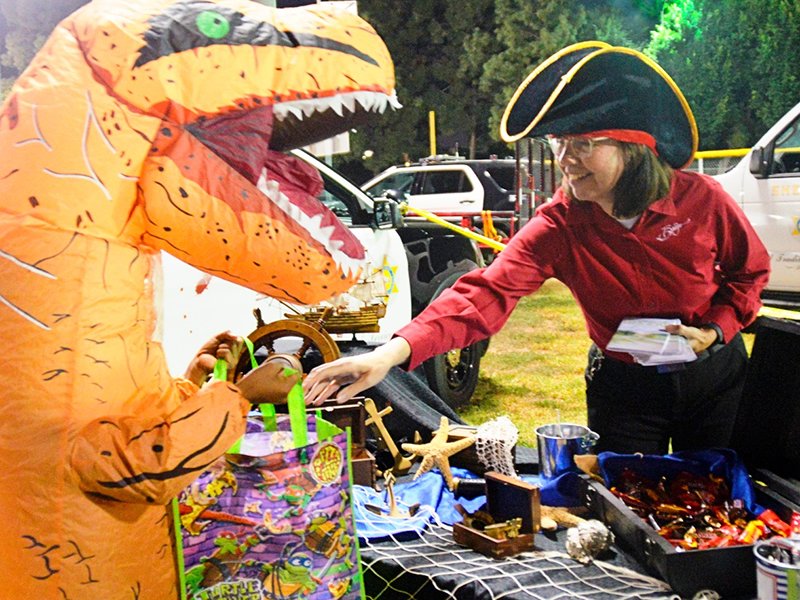 Bridge volunteers place sweets and The Way to Happiness in the trick-or-treat bag of a friendly dragon at the East L.A. Sheriff’s Department “Trunk or Treat“ celebration.